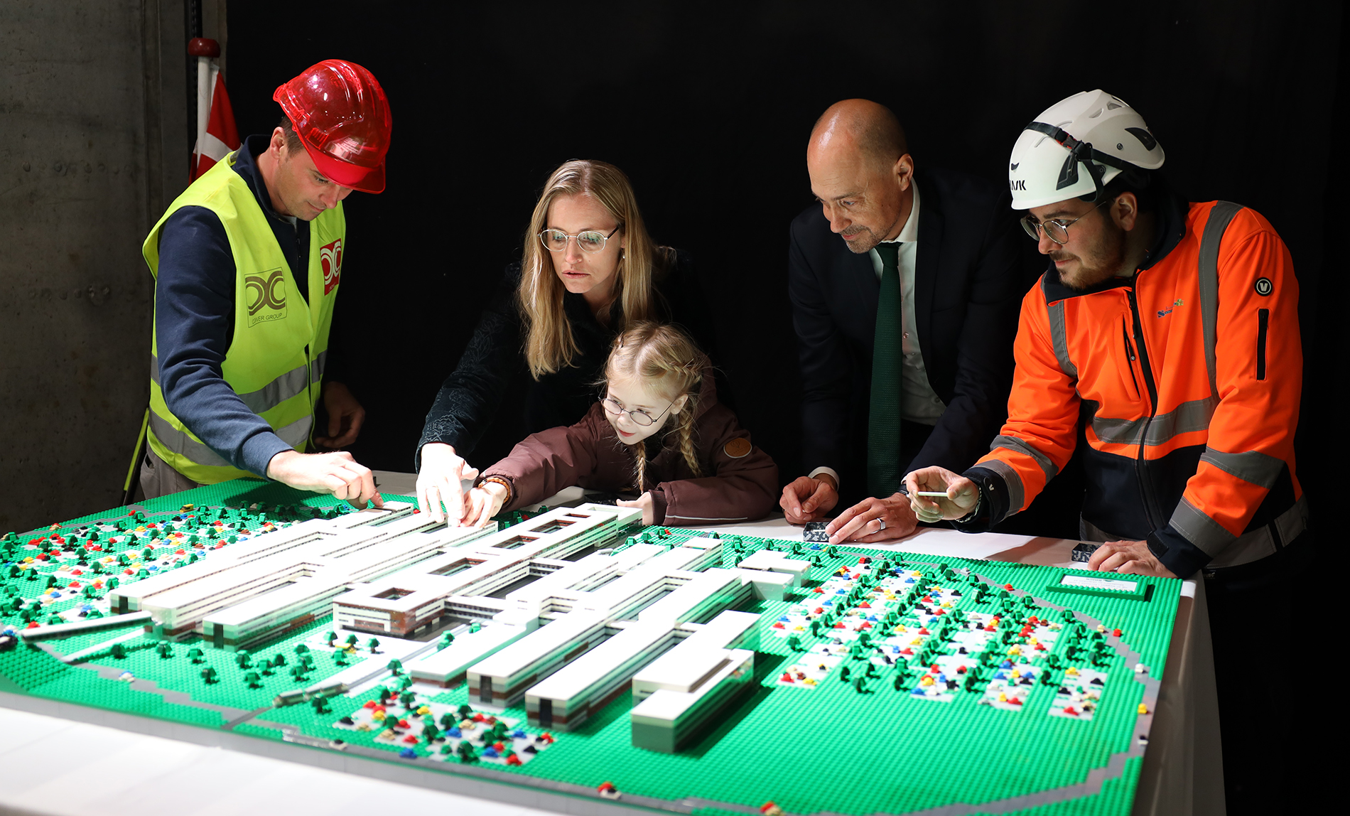 Regionsrådsformand Stephanie Lose, 9-årige Silje og sundhedsminister Magnus Heunicke flankeret af to håndværkere fra byggepladsen sætter de sidste klodser på en LEGO-model af det nye OUH. Silje er patient på H.C. Andersens børnehospital på OUH