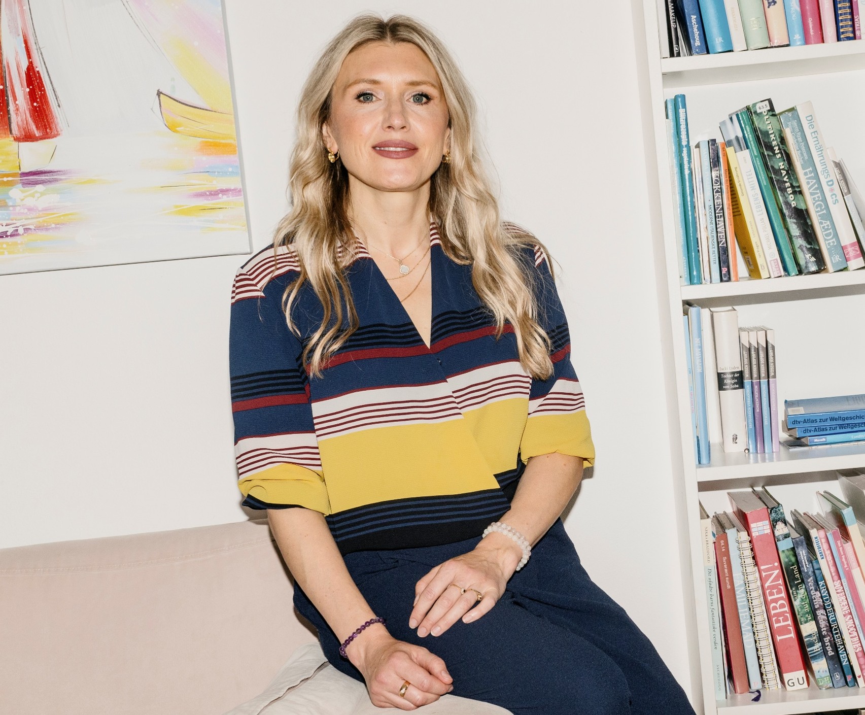 Lektor Aida Bikic sidder på armlænet af en sofa.